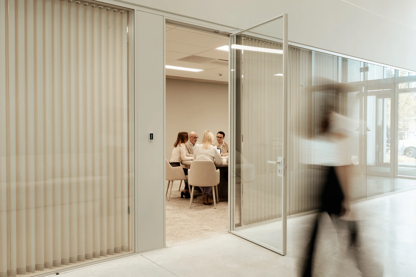 Overleg in de glazen vergaderruimte, met een collega die voorbijloopt